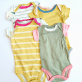 تصویر مجموعهای از چهار بادی نوزادی تیکهدوزی شده با طرحهای متنوع (راهراه، درخت، ساده) و رنگهای شاد (زرد، سبز، صورتی، کرم) روی زمینه سفید، مناسب برای سنین ۰ تا ۶ ماه